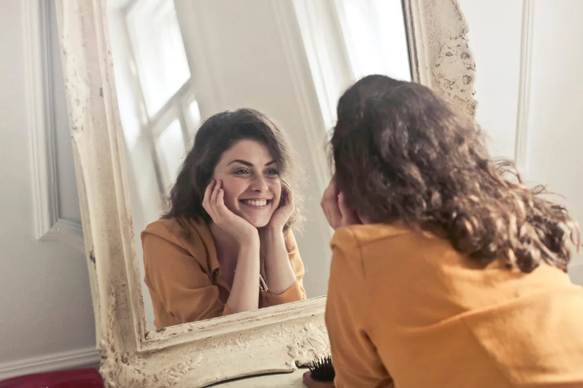 Mujer morena mirándose al espejo y sonriendo como símbolo de cómo mejorar la autoestima y fortalecer el bienestar emocional.