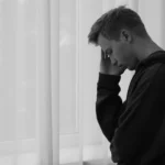 Hombre pensativo junto a la ventana, mostrando preocupación y reflexión, ilustrando los síntomas de depresión y la introspección emocional.